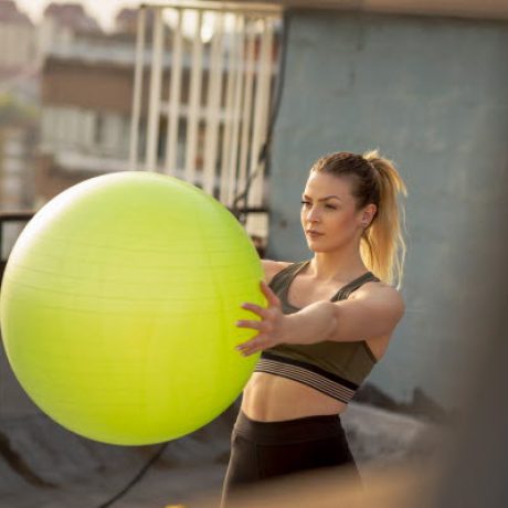Woman standing on a building rooftop terrace, working out with a pilates ball